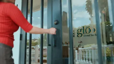 Hand opening the glass front door of Glo Dental Studio