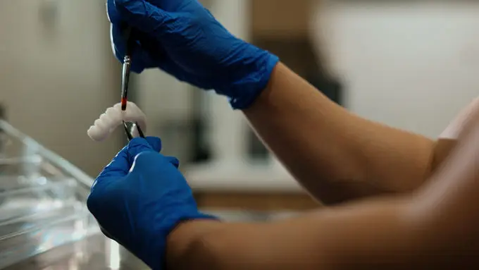 Gloved hands holding a dental instrument and a tooth restoration
